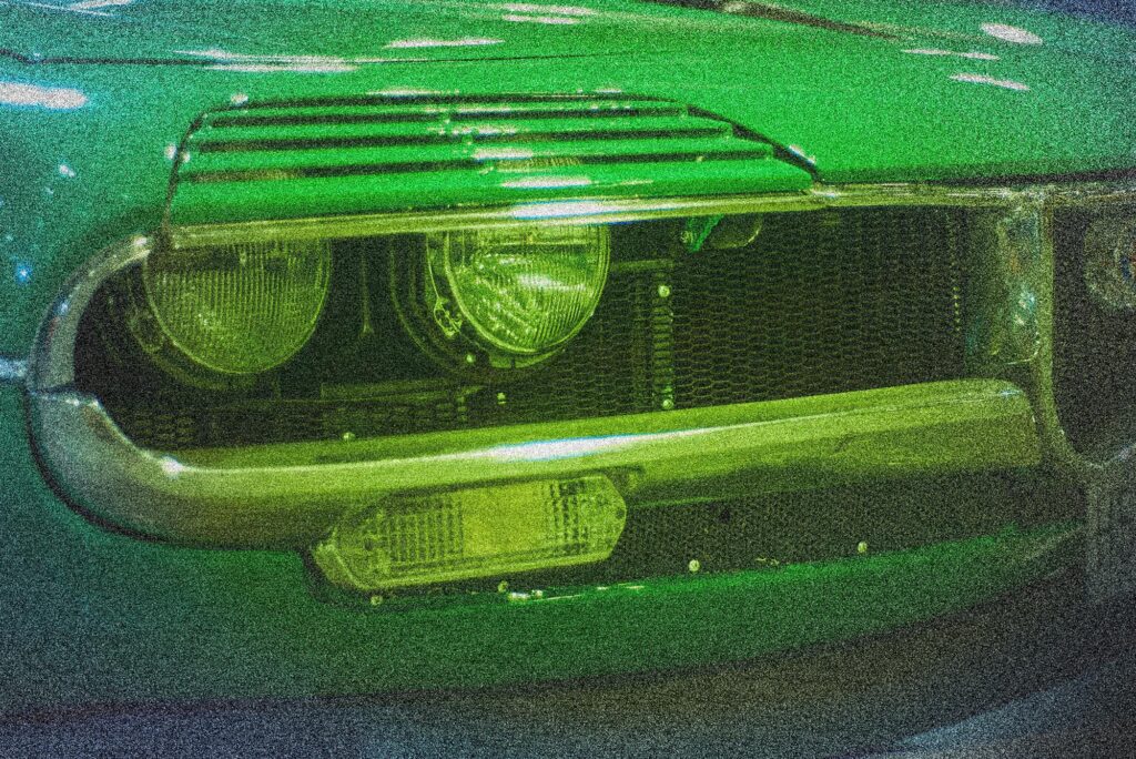 Detalle de faros delanteros dobles de un Alfa Romeo GT Junior clásico bajo luz verde ambiental - Frameburn