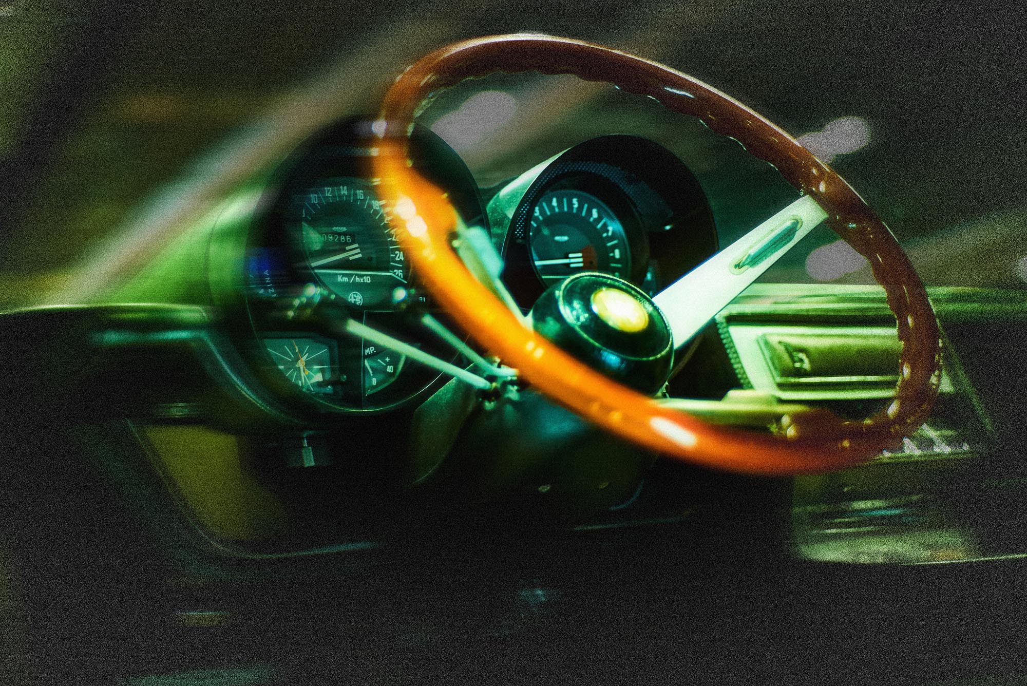 Volante de época visto a través del parabrisas de un Alfa Romeo GT Junior con reflejo de luz verde - Frameburn